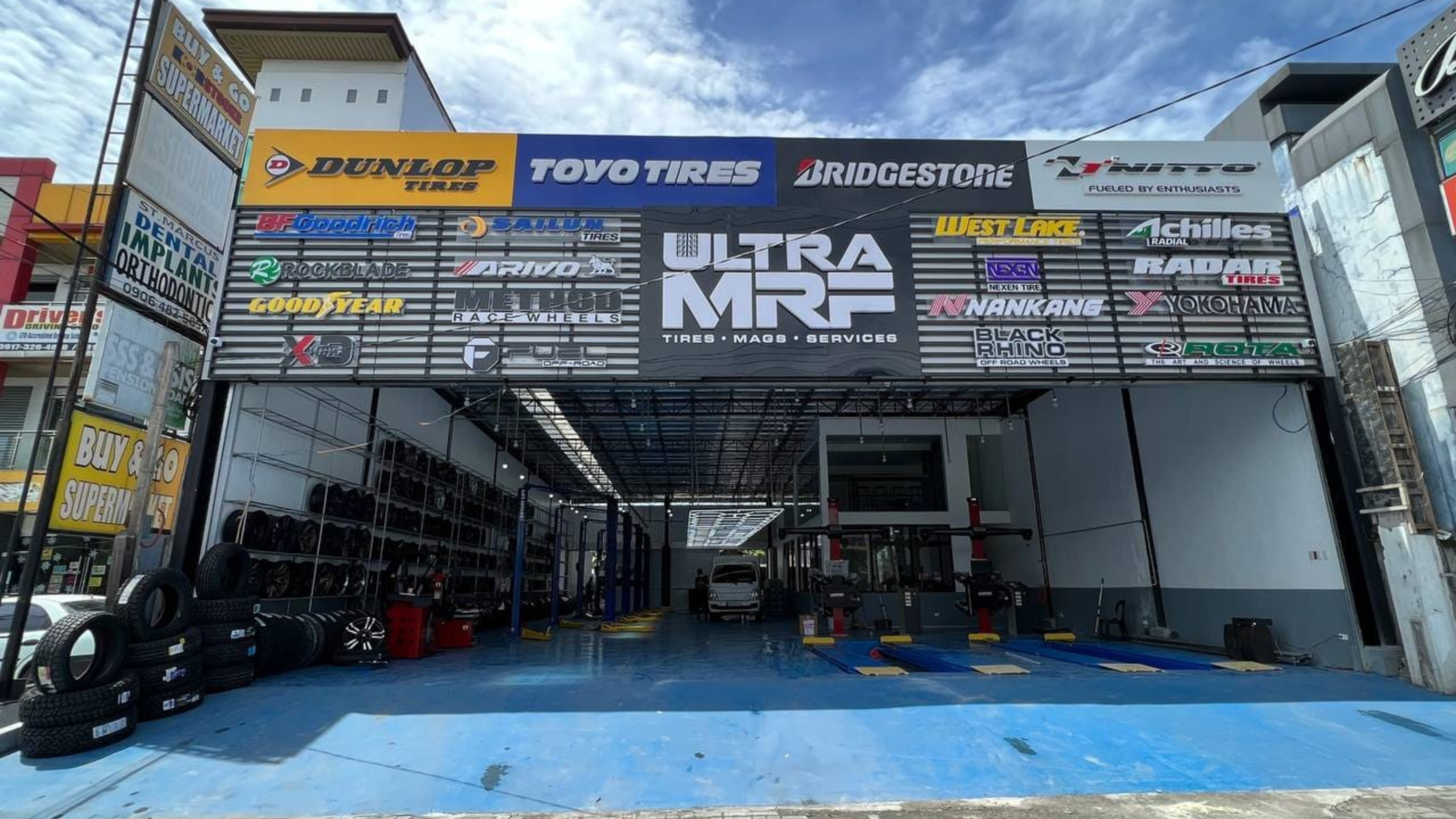 Ultra MRF Tire Shop entrance displaying an array of branded tire banners including Dunlop, Toyo Tires, Bridgestone, and Goodyear and offering Car Care Services.