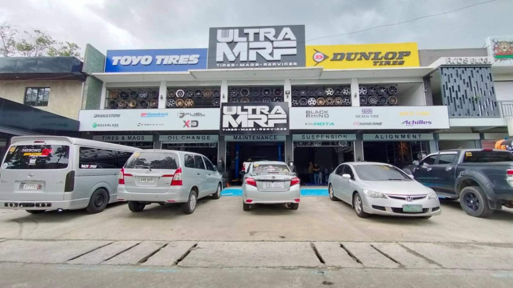 Front view of Ultra MRF tire shop with several vehicles parked in the driveway, showcasing prominent signage of brands like Toyo Tires and Dunlop Tires and offering Car Care Services.