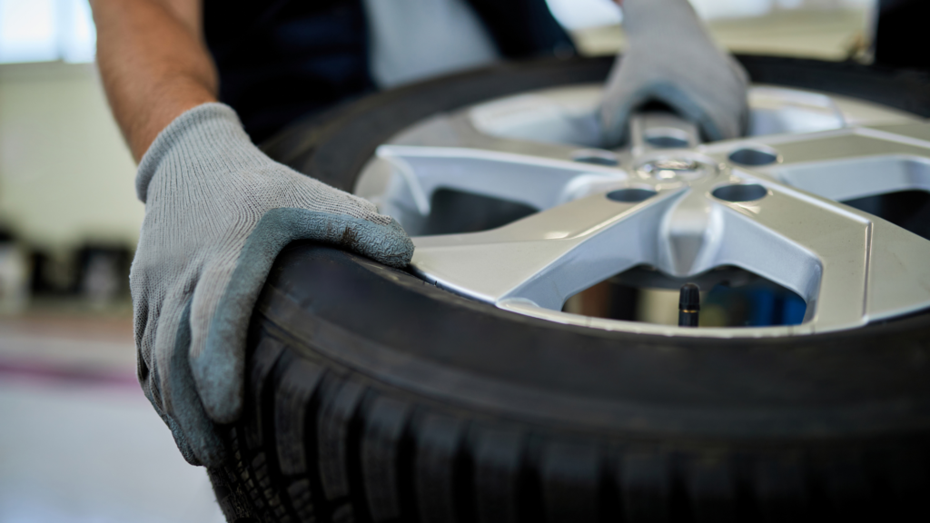 Mechanic wearing gray gloves handling a car tire with a silver alloy wheel.