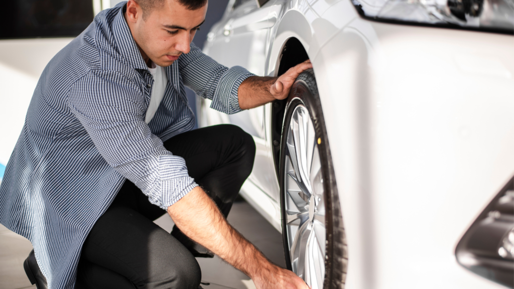 A man inspecting a car tire, ensuring proper condition and alignment.